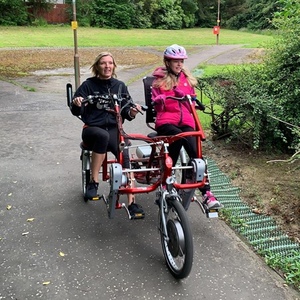 a woman and a young girl riding an adaptive bike together in the park